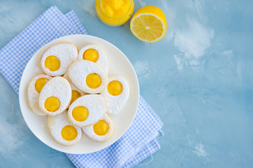 Easter cookies in the form of Easter egg with powdered sugar and lemon cream on a white plate on a light blue concrete background. A greeting card. Easter background. Horizontal, Copy space. Top view.