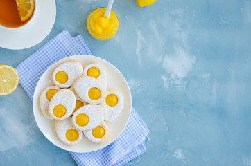Easter cookies in the form of Easter egg with powdered sugar and lemon cream on a white plate on a light blue concrete background. A greeting card. Easter background. Horizontal, Copy space. Top view.