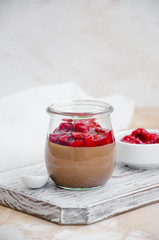 Italian dessert - chocolate panna cotta, mousse, cream or pudding with cherry sauce in a glass jar on a board on a light concrete background. Vertical orientation. Copy space
