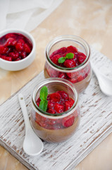 Italian dessert - chocolate panna cotta, mousse, cream or pudding with cherry sauce in a glass jar on a board on a light concrete background. Vertical orientation. Copy space