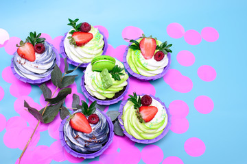cupcakes with whipped cream decorated chocolate bar, strawberry ,macaroons on blue background. Picture for a menu or a confectionery catalog. with space for text. decorated with pink confetti.