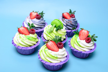 cupcakes with whipped cream decorated chocolate bar, strawberry ,macaroons on blue background. Picture for a menu or a confectionery catalog. with space for text.