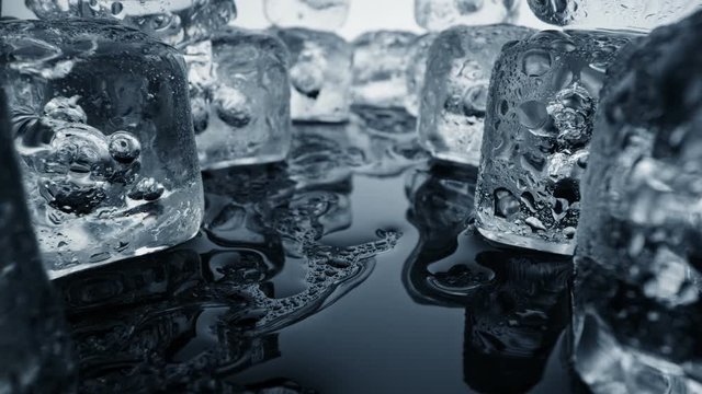 Ice melting. Camera moving through ice cubes and puddles of water on black background. Extreme heat and climate change concept