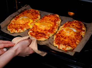 Khachapuri. A traditional Georgian dish with cheese, cottage cheese and eggs. Bakery products. A woman takes a dish out of the oven.