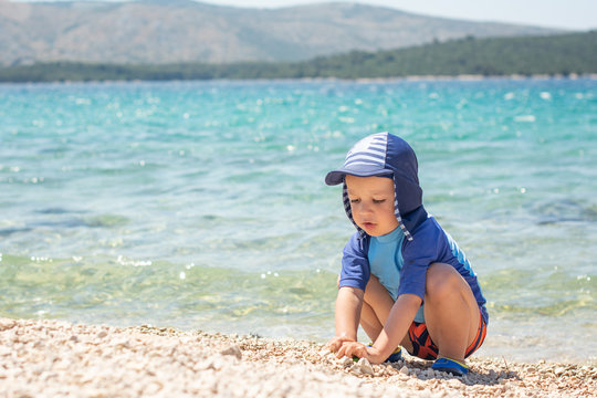 cute little boy waering sun hat and spv protective clothes swimming wear  playing on a beach summer holiday on a beach by a sea in croatia 