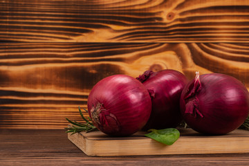 Red or purple onions with basil and rosemary leaves on a cutting board, wooden background with copy space. Fresh vegetables for healthy eating