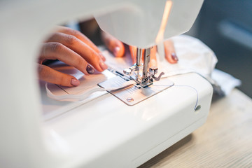 Young female hands on a sewing machine. Girl sews stylish little things at home.