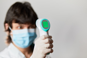 Doctor wearing protective  mask ready to use infrared forehead thermometer  to check body...