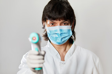 Doctor wearing protective  mask ready to use infrared forehead thermometer  to check body...