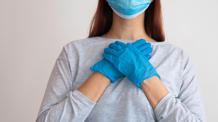 Fototapeta premium Woman with a surgical mask holding her hands in latex glove on her heart.