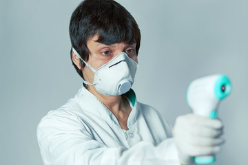 Doctor wearing a respirator N95 mask to use infrared forehead thermometer  to check body...