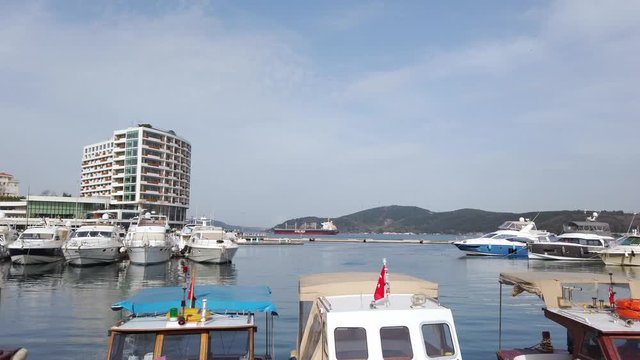 clear sunny warm day. Private yachts and sailing boats with lowered sails standing on pier in bay. Reflections in water. People walk along promenade. Turkey, Istanbul, Tarabya, February 2020.