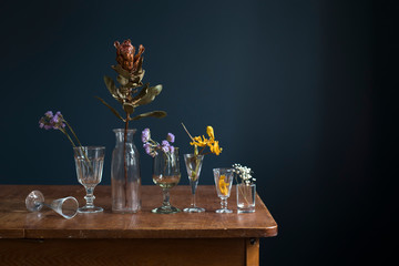 Dried flowers in glass glasses on a wooden table opposite a dark blue wall