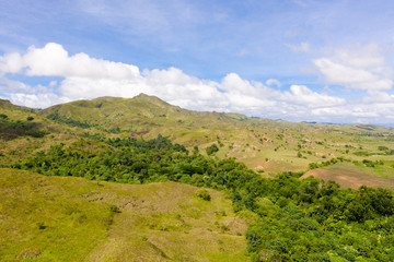 Green hills and blue sky with clouds. Beautiful landscape on the island of Luzon, aerial view.
