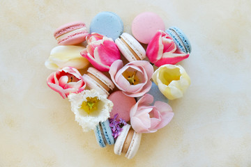 Feminine composition with traditional french macarons sweets and tender tulip flowers on yellow grunged concrete textured background. Top view, close up, copy space.