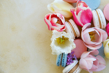 Feminine composition with traditional french macarons sweets and tender tulip flowers on yellow grunged concrete textured background. Top view, close up, copy space.