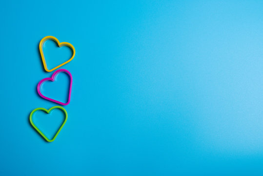 Three colored cookie cutters for making cookies in the form of hearts on a blue background. Culinary concept. Flat lay with copyspace.