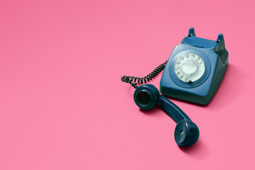 Blue vintage antique rotary phone on a pink background with lifted handset receiver with copy space...