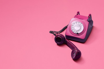 Pink vintage antique rotary phone with lifted handset receiver on a pink background with copy space...
