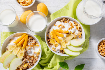 Granola and vegetarian yogurt with slices of apple, apricot, banana and a jug of milk on a white wooden background. Healthy breakfast concept. Top view
