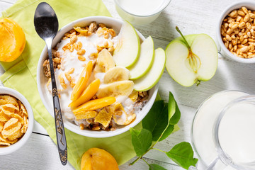 Granola and vegetarian yogurt with slices of apple, apricot, banana and a jug of milk on a white wooden background. Healthy breakfast concept. Top view