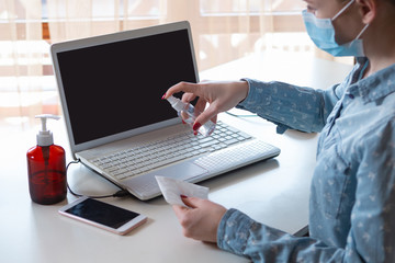 Way to keep it safe. Young woman disinfecting gadgets surfaces on her workplace. Working out with laptop, smartphone, using sanitizer. Prevention against pneumonia, COVID-19 spreading, protecting.