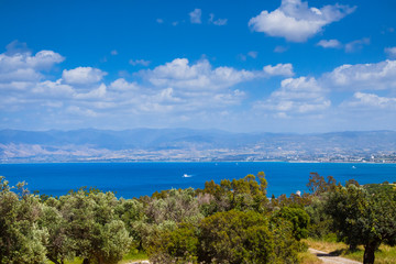 Fototapeta na wymiar Summer seascape on Cypus. View to the bay with green grove in front and blue clouded sky. View from the hill. Latchi village on other side of the bay.