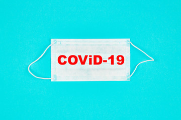 A close up of medical mask on blue background with text covid-19. Coronavirus protection. Copy paste for text. Top view. Flat lay.