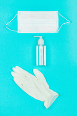 Medical mask, white latex gloves and hand sanitizer gel on blue background. Coronavirus protection. Top view. Flat lay.