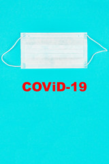 A close up of medical mask on blue background with text covid-19. Coronavirus protection. Copy paste for text. Top view. Flat lay.