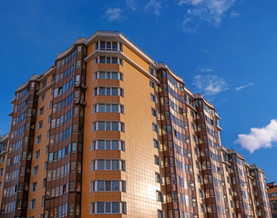 Modern residential building against the blue sky. The building has yellow walls and brown balconies