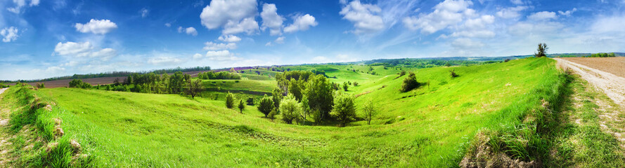 Fototapeta na wymiar Panorama of hilly landscape with bright blue cloudy sky