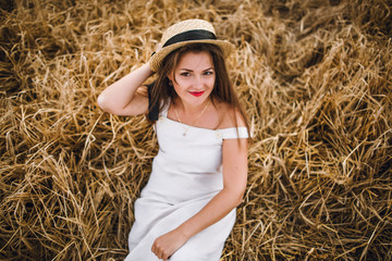 Naklejka na ściany i meble beautiful girl in a hat with brunette hair on a wheat field background. warm summer time. 