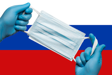 Medic holding respiratory face mask in hands in blue gloves on background flag of Russian Federation. Concept coronavirus quarantine, grippe, pandemic outbreak. Medical respiratory bandage for face.