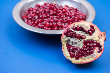 Pomegranate grains in a metal plate and half ripe pomegranate on a blue background