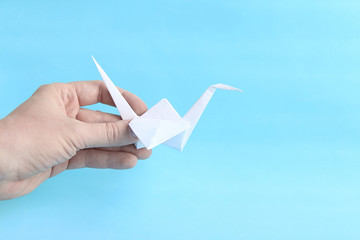 Handmade white origami paper crane (or orizuru) in person's hand on the blue background. Symbol of...