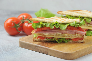 Classic club sandwich on a wooden tray.  The delicious sandwich filling consists of ham, cheese, sliced ​​tomato, lettuce and sauce.  In the background are tomatoes and lettuce.  Close-up.