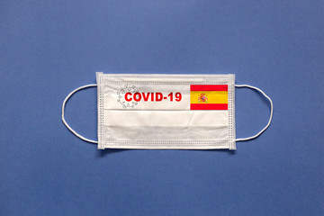 Flag of Spain and inscription COVID-19 on a medical mask on a blue background. Healthcare and medical concept. Pandemic virus COVID-19