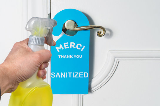 Hand Holding A Disinfectant Bottle Spray To Sanitize A Door Knob With Thank You Tag