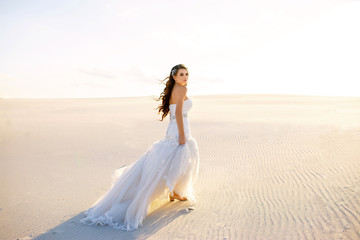 Fototapeta na wymiar a beautiful bride in a beautiful long dress walks on the sand in the desert