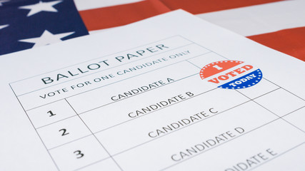 Man hand marks selected candidate with I Voted Today sticker on a paper ballot for US Presidential Elections.