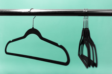Close-up of clothes rack with black empty hangers on background of aqua menthe color.