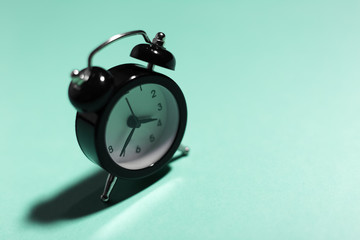 Close-up of black alarm clock on background of aqua menthe color.
