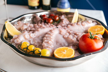 Cooked gourmet octopus with tomato lemon and ice, side view, horizontal, white table