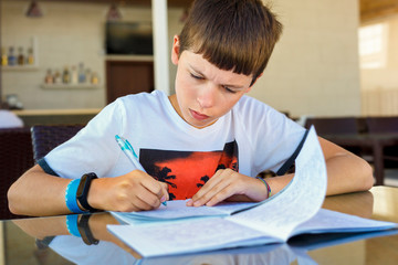 Naklejka premium Preteen schoolboy doing his homework. Education and distance learning for kids. Homeschooling during quarantine. Stay at home entertainment.