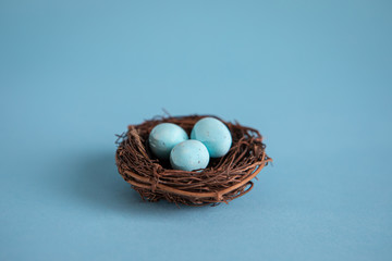 Three blue easter eggs in a bird's nest on a blue background