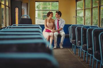 A guy and a girl in retro clothes with vintage hairstyles sit inside an old tram