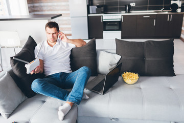Young man watch tv in his own apartment. Guy sit on couch and talking on phone. Hold wi-fi router...
