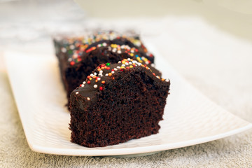 homemade Cocoa cake with chocolate flavored icing and colorful sprinkles, placed on a white porcelain tray