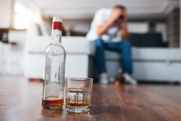 Young man watch tv in his own apartment. Picture with blurred background where guy sit on couch and suffer from hangover or headache. Alcoholic has troubles with drinking strong drinks.